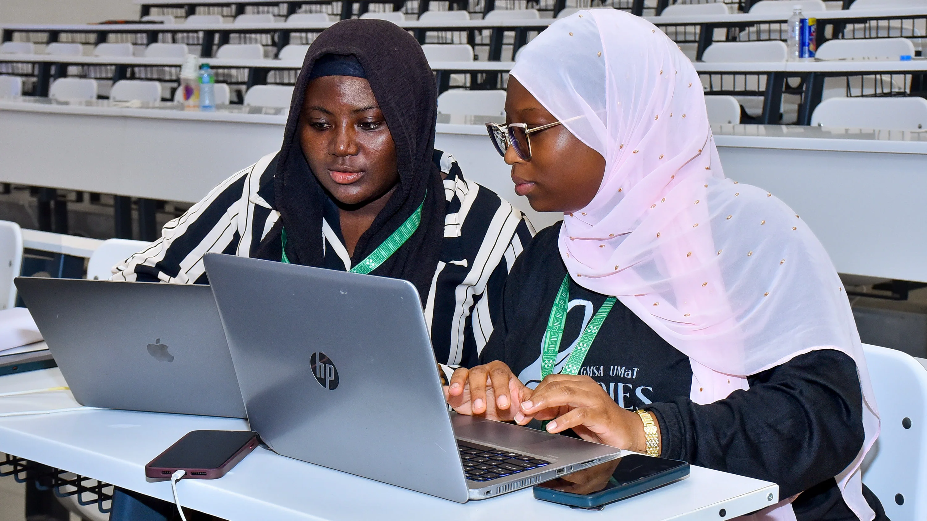 two women collaborating on their laptops in a lecture hall